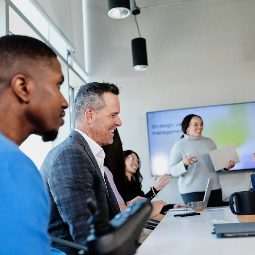 Colleagues sit together in a conference room during a presentation on a screen.