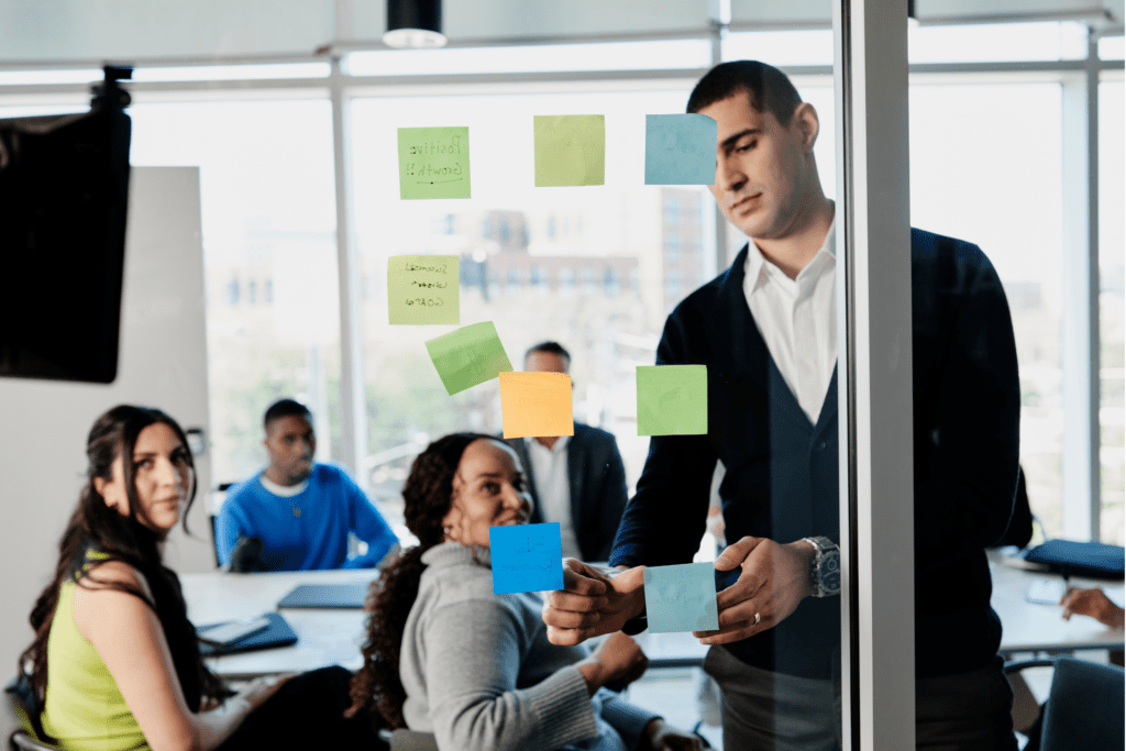 Man puts up sticky notes on the wall in front of onlookers in a conference room