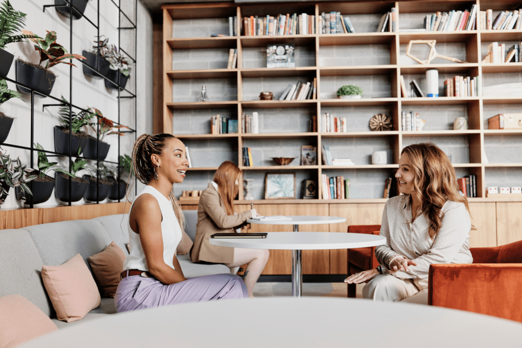 Two women sitting at a table in an office common area.